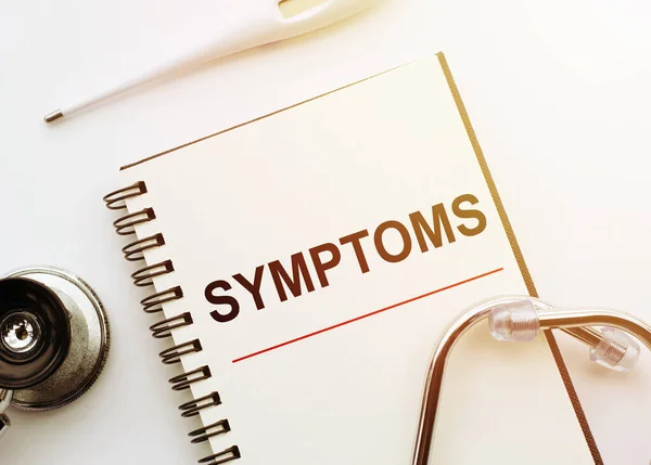 医学概念 带有Symptoms字样的笔记本 白色桌子上有听诊器和温度计 — 图库照片