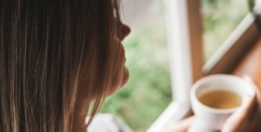 Bir fincan çayla pencerenin yanındaki kadın. Hayal et ve rahatla.