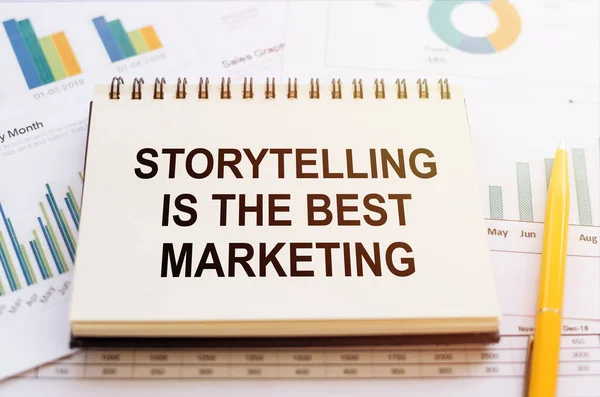 STORYTELLING IS THE BEST MARKETING - written on notepad on financial charts and graphs with yellow pen.