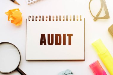 Ofis araçlarıyla birlikte beyaz masadaki defterde AUDIT metni.