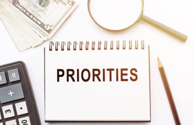 Beyaz üzerine izole edilmiş kalem, hesap makinesi, büyüteç ve dolar ile el yazması öncelikleri listesi.