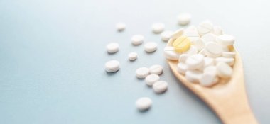 Beyaz tabletler mavi zemin üzerinde ahşap kaşıkta bir sarı üzerinde.