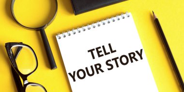 Yazılı not: Sarı arkaplan, gözlük, büyüteç ve kurşun kalemle hikayenizi anlatın. İş konsepti.