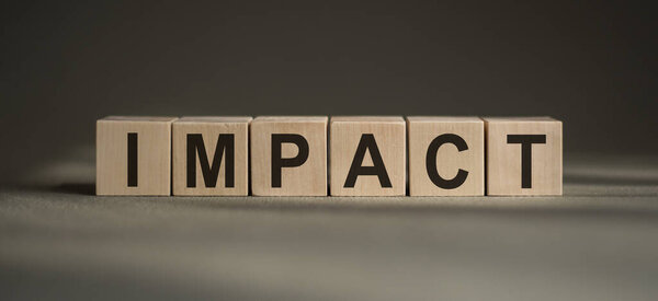 A wooden blocks with the word IMPACT written on it on a gray background.