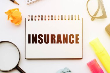 Ofis araçlarıyla birlikte beyaz masadaki defterde INSURANCE metni.