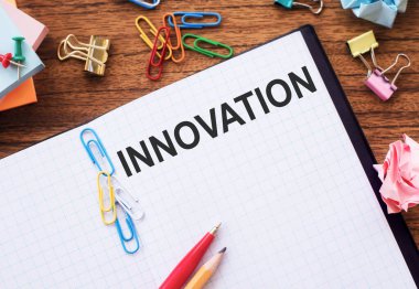 Çubuklu, renkli ataçlı ve buruşuk çarşaflı bir masanın üzerinde metin INNOVATION içeren defter.