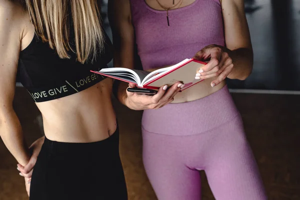 Spor giyimli iki narin kız yoga yapıyor ve kitap okuyor.