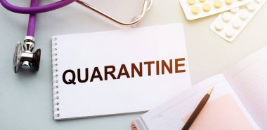 Stetoskop, haplar ve defter. Tıp masasında QuarANTINE kelimesi var..