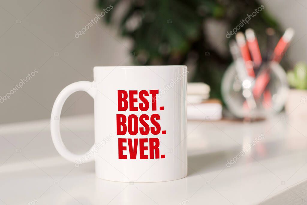 Coffee mug with text BEST. BOSS. EYER. in workplace background.