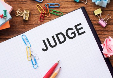 Masanın üzerinde renkli ataçlar ve buruşuk kağıtlarla JUDGE metni olan not.