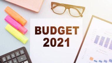 Hesap makinesi, keçeli kalem, gözlük ve mali tablolarla ofis masasında bulunan metin BUDGet 2021.