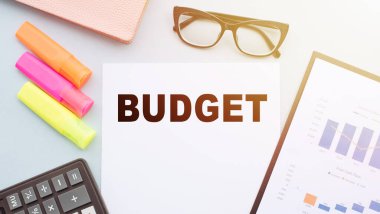 Hesap makinesi, keçeli kalemler, gözlükler ve mali tablolarla ofis masasındaki metin.