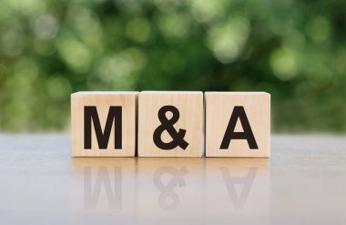 Tahta bloklara yazılmış M & A (Birleştirme ve Satın Alma) kelimesi. Metin siyah harflerle yazılır ve masanın ayna yüzeyine yansıtılır. Tasarımınız için iş kavramı.