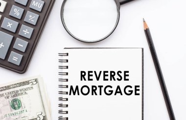 Hesap makinesi, dolar ve büyüteçle birlikte üzerinde REVERSE MortGage notu olan not defteri.