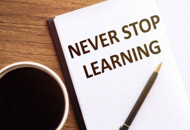 Asla öğrenmeyi bırakma - Ahşap masadaki not defterine yazılmış metin.