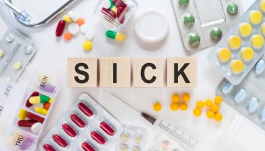 Hastasın. Masadaki tahta bloklar hakkında. Arka planda haplar, vitaminler, steteskop ve şırınga ile tıbbi konsept.