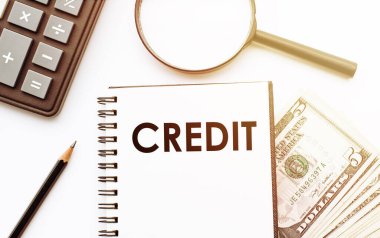 Dolar ve ofis araçlarının arka planında CREDIT metni olan beyaz not defteri.