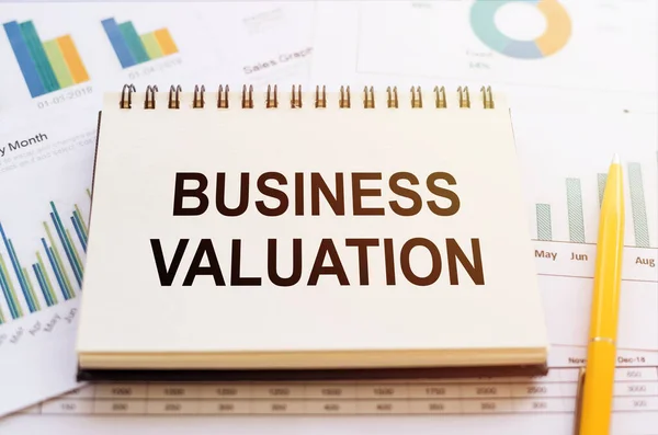 BUSINESS VALUATION - written on notepad on financial charts and graphs with yellow pen.
