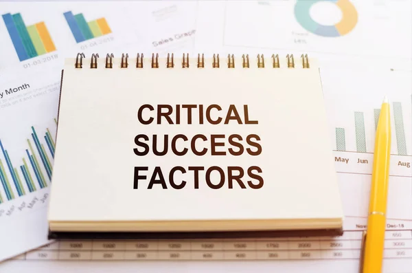 CRITICAL SUCCESS FACTORS - written on notepad on financial charts and graphs with yellow pen.