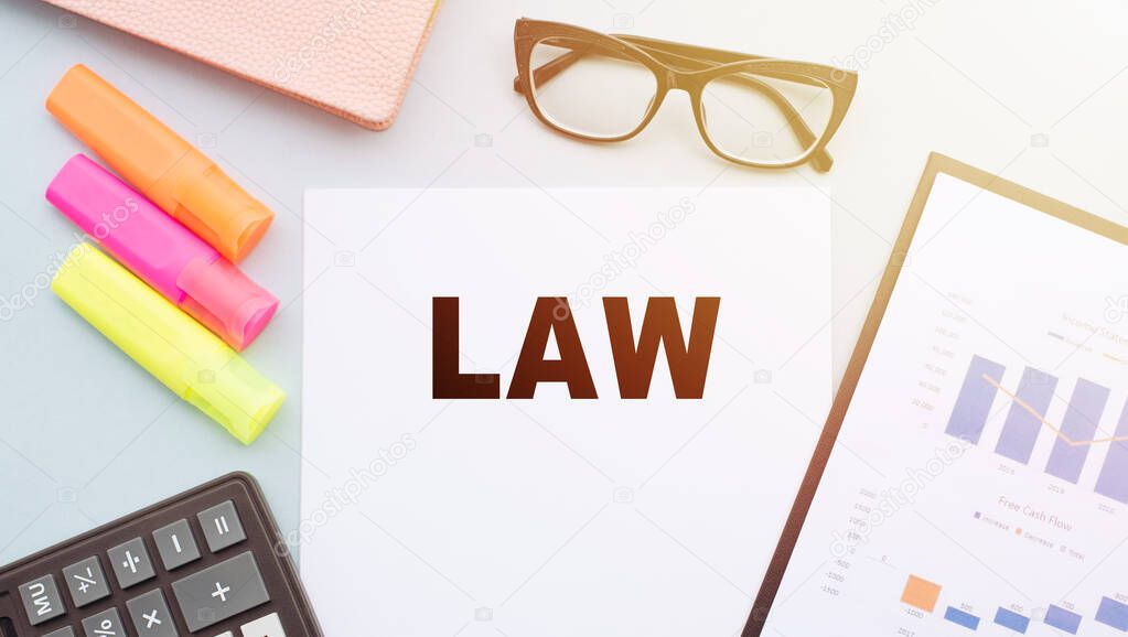 The text LAW on office desk with calculator, markers, glasses and financial charts.