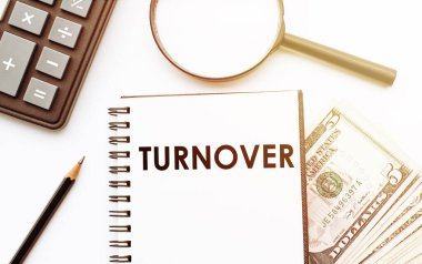 Dolar ve ofis araçlarının arka planında TURNOVER metni olan beyaz not defteri.