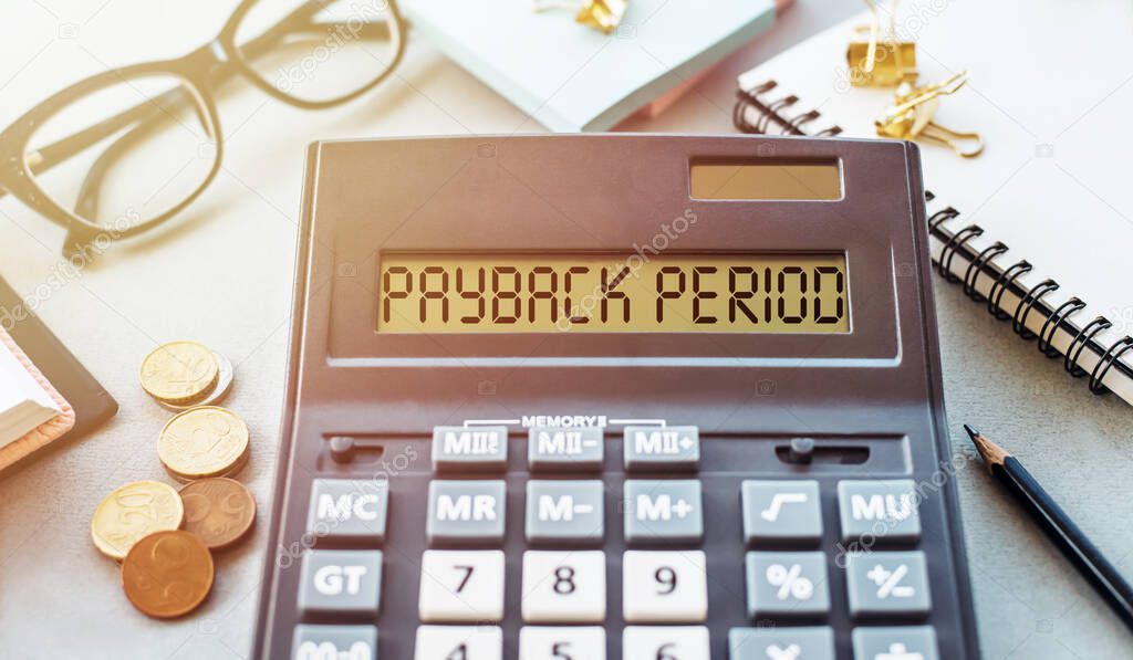 Word PAYBACK PERIOD written on calculator on office table.