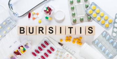 Masadaki tahta bloklardaki BURSITIS ilaç sözcüğü. Arka planda haplar, vitaminler, steteskop ve şırınga ile tıbbi konsept.