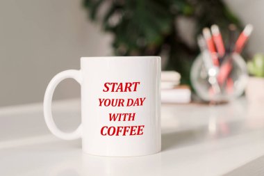 Coffee mug with text - Start your day with coffee in workplace background.