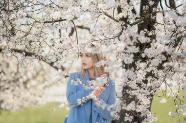 Pretty young woman while standing under branches of blooming tree on calm spring day in garden