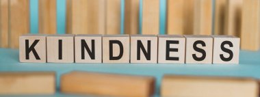 KINDNESS - açık mavi arkaplanda tahta bloklar üzerine yazılmış kelime.