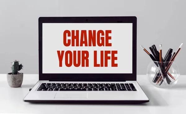 Laptop with text CHANGE YOUR LIFE on modern office background.