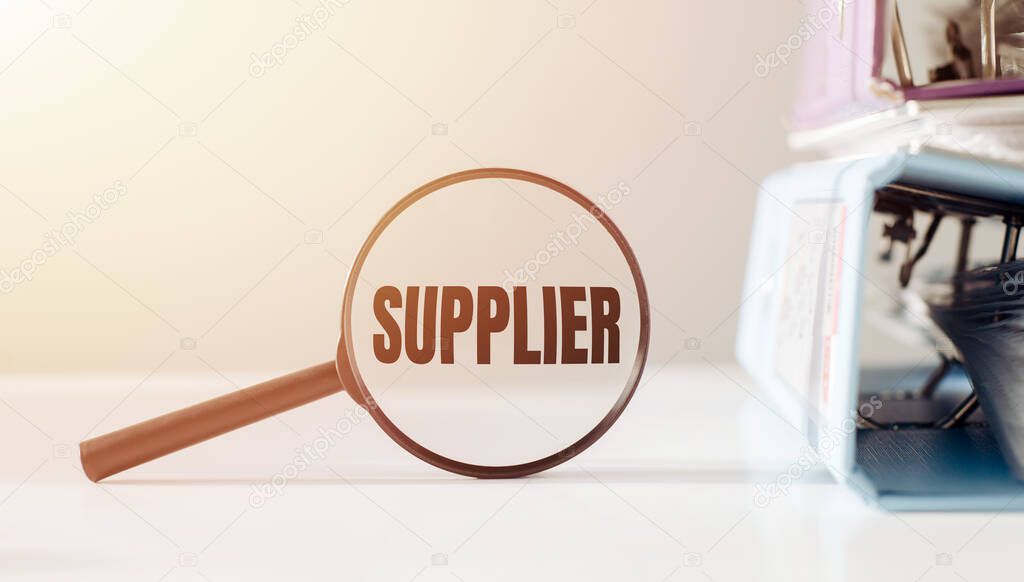 Magnifying glass with the word SUPPLIER on office table.