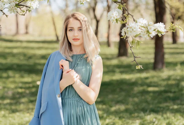 Portret Pięknej Blondynki Zielonej Sukience Niebieskim Płaszczu Wśród Kwitnących Jabłoni — Zdjęcie stockowe