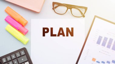 Hesap makinesi, işaretleyiciler, gözlükler ve mali tablolarla ofis masasındaki metin..