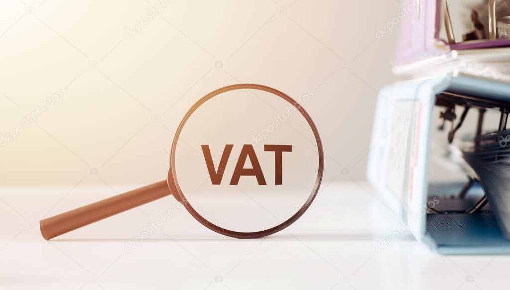 Magnifying glass with the word VAT on office table.