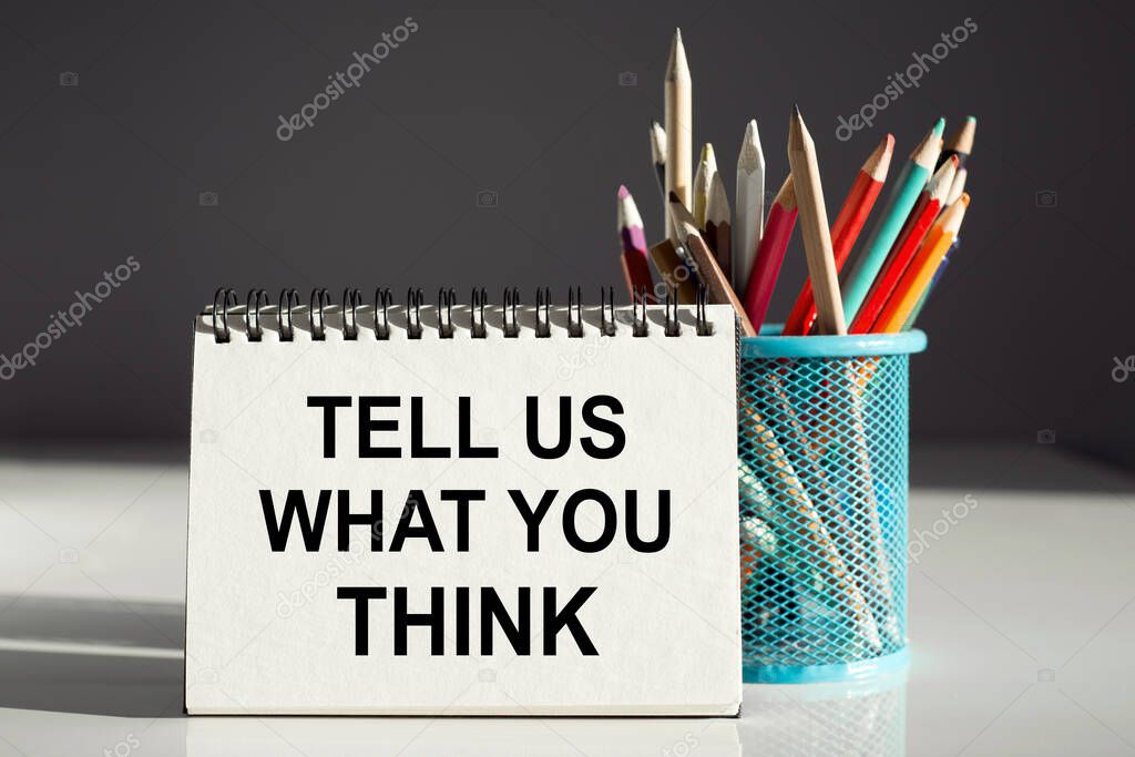 TELL US WHAT YOU THINK - inscription on a notebook with colored pencils.