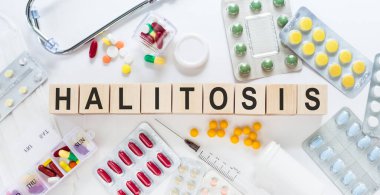 Masadaki tahta bloklarda HALITOSIS kelimesi. Arka planda haplar, vitaminler, steteskop ve şırınga ile tıbbi konsept.