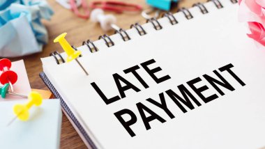 LATE PAYMENT - text on a notepad with wrinkled paper and paper needles on wooden background.