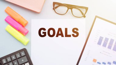 The text GOALS on office desk with calculator, markers, glasses and financial charts.