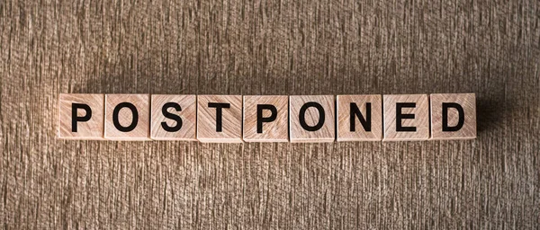 POSTPONED - word written on wooden blocks on a brown background.
