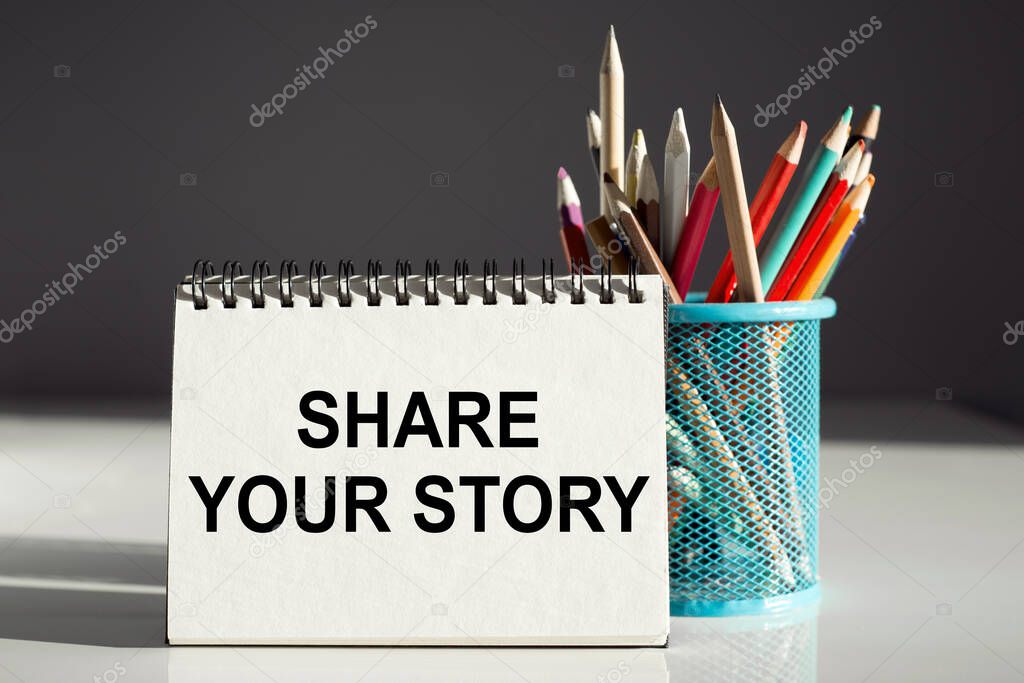 SHARE YOUR STORY - inscription on a notebook with colored pencils.