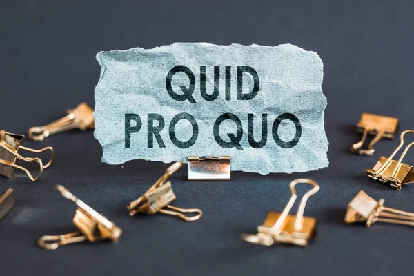 Gri arkaplanda klipsleri olan mavi bir kağıt parçası Quid Pro Quo.