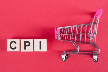 CPI sözcüğü - Müşteri Fiyat Endeksi, ahşap küplerde, pembe bir arka planda, alışveriş arabasıyla.
