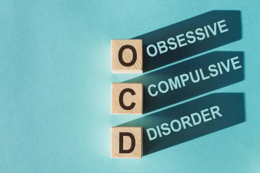 Wooden cubes building word OCD - (abbreviation Obsessive Compulsive Disorder) on light blue background. clipart