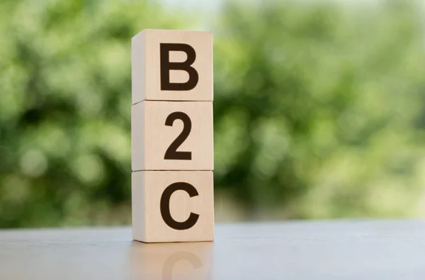 The word B2C (abbreviation of business to consumer) built from wooden cubes outdoors on the background of nature.