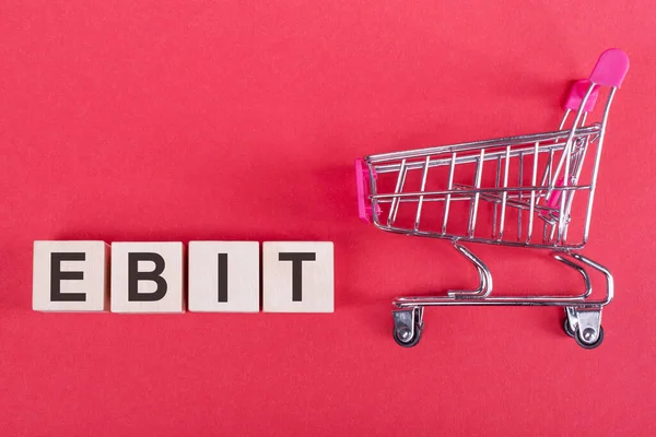 Das Wort Ebit Auf Holzwürfeln Auf Rosa Hintergrund Mit Einkaufswagen — Stockfoto