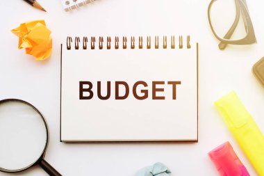 Metin Bütçesi beyaz masadaki defterde ofis araçlarıyla birlikte.