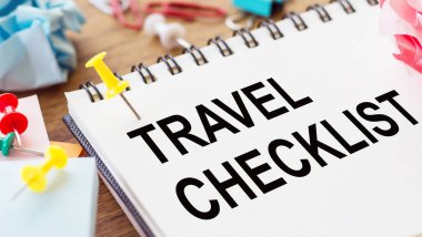 TRAVEL CHECKLIST - Ahşap zemin üzerinde buruşuk kağıt ve kağıt iğneler ile bir not defteri üzerinde metin.