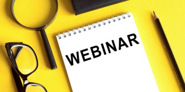 Sarı arkaplan, gözlük, büyüteç ve kurşun kalemle birlikte WEBINAR yazılı not defteri. İş konsepti.