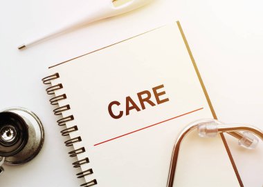 Medical concept. Notebook with word CARE on white desk with stethoscope and thermometer.